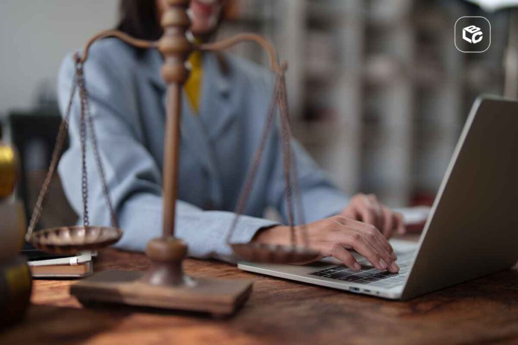 Advogada trabalhando no laptop ao lado da balança da justiça, em processo concluído para despacho.