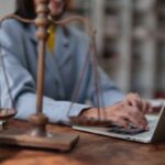 Advogada trabalhando no laptop ao lado da balança da justiça, em processo concluído para despacho.